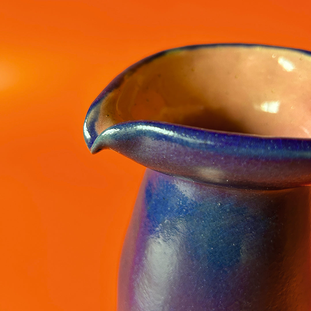 Detailaufnahme von einem handgefertigten blauen Krug auf orangem Hintergrund inspiriert von peruanischen präkolumbischen Formen.