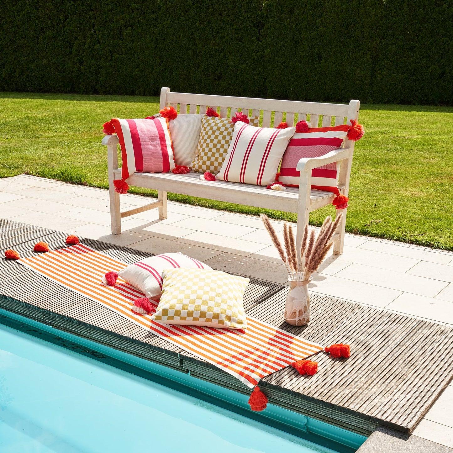 Sitzbank mit pinkigen Kissen neben blauem Pool