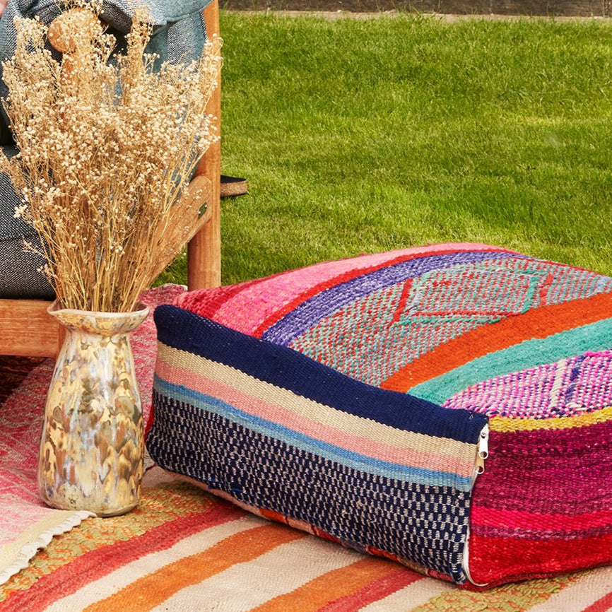 Krug mit trockenblumen auf einer Wiese neben einem farbigen südamerikanischen Sitzpouff