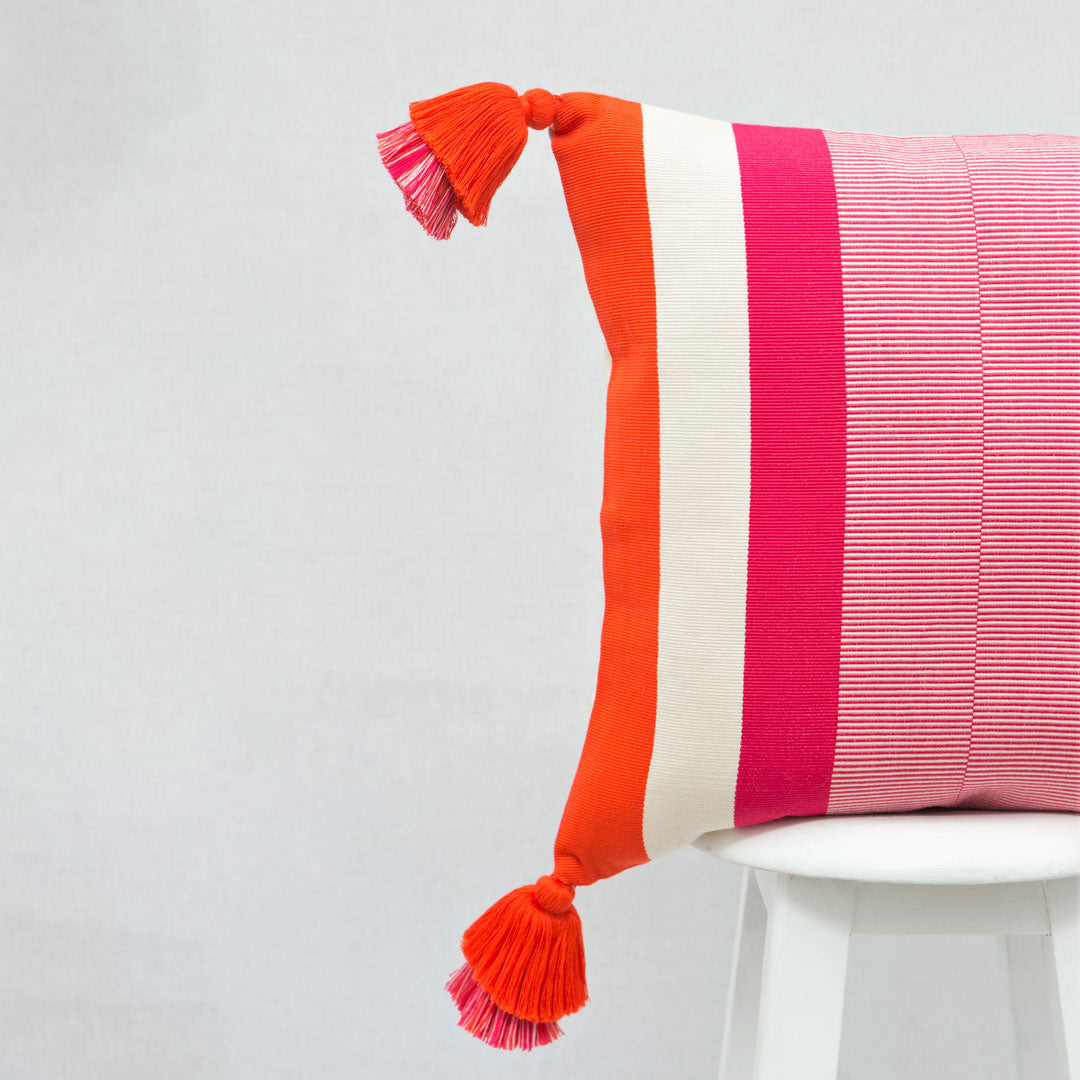 Von Hand gewobenes Kissen mit modernem pink und orangem Linienmuster und mit Tasseln.