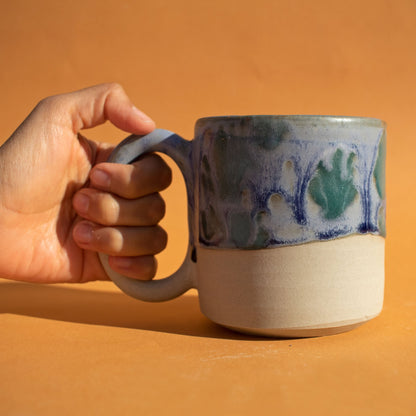 Hand hält eine Handgefertigte blaue Tasse inspiriert von peruanischen präkolumbischen Formen.